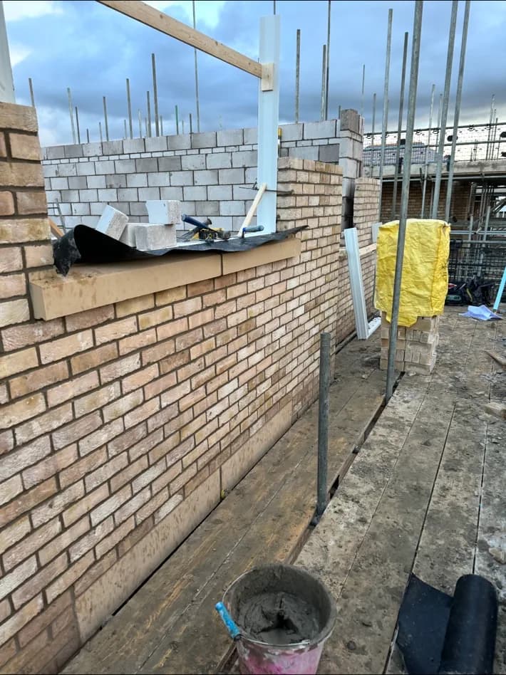 Cream-brick outer leaf built to a level course beside blockwork, with a lintel bedded over a new opening